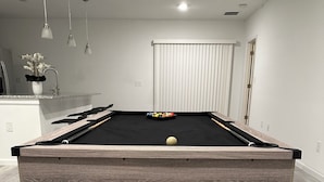 Een pooltafel met houten frame en zwart vilt, op een licht houten vloer in een ruimte met witte wanden en een deur op de achtergrond.