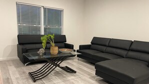Een moderne woonkamer met een zwarte modulaire bank, een glazen salontafel en een potplant.