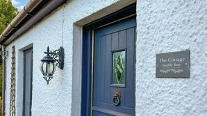 Un edificio blanco con una puerta azul y un letrero que dice 'The Cottage Smiddy Brae'.