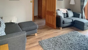 Una sala de estar con un sofá gris, un sofá azul, una puerta de madera y una alfombra gris.