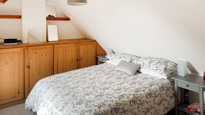 Un dormitorio con colcha estampada, un armario de madera, una mesita de noche con lámpara y una mesita auxiliar.