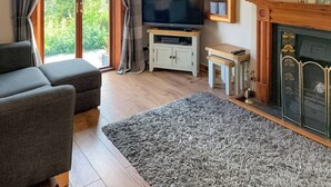 Una sala de estar con sofá, televisor sobre un mueble, chimenea y vista a zonas verdes.