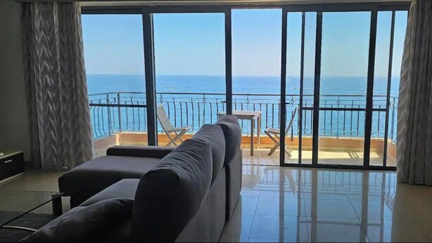 A balcony with a view of the sea, a sofa, and a table.