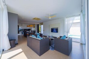 Una sala de estar moderna con un conjunto de sofás, un televisor y un comedor al fondo.