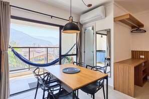 Un espace repas avec une table en bois, des chaises noires, un hamac suspendu et une vue sur les montagnes grâce à de grandes fenêtres.