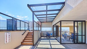 A modern outdoor patio area with a glass enclosure, a staircase, and a dining table with chairs. - Matira Beach 114 (Ubatuba)