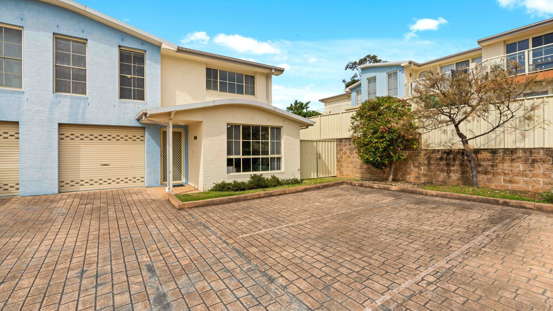 A residential property with a paved driveway, a garage, and a small front yard with a tree.