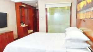 Habitación de hotel con cama, televisión, espejo y puerta que da a un baño.