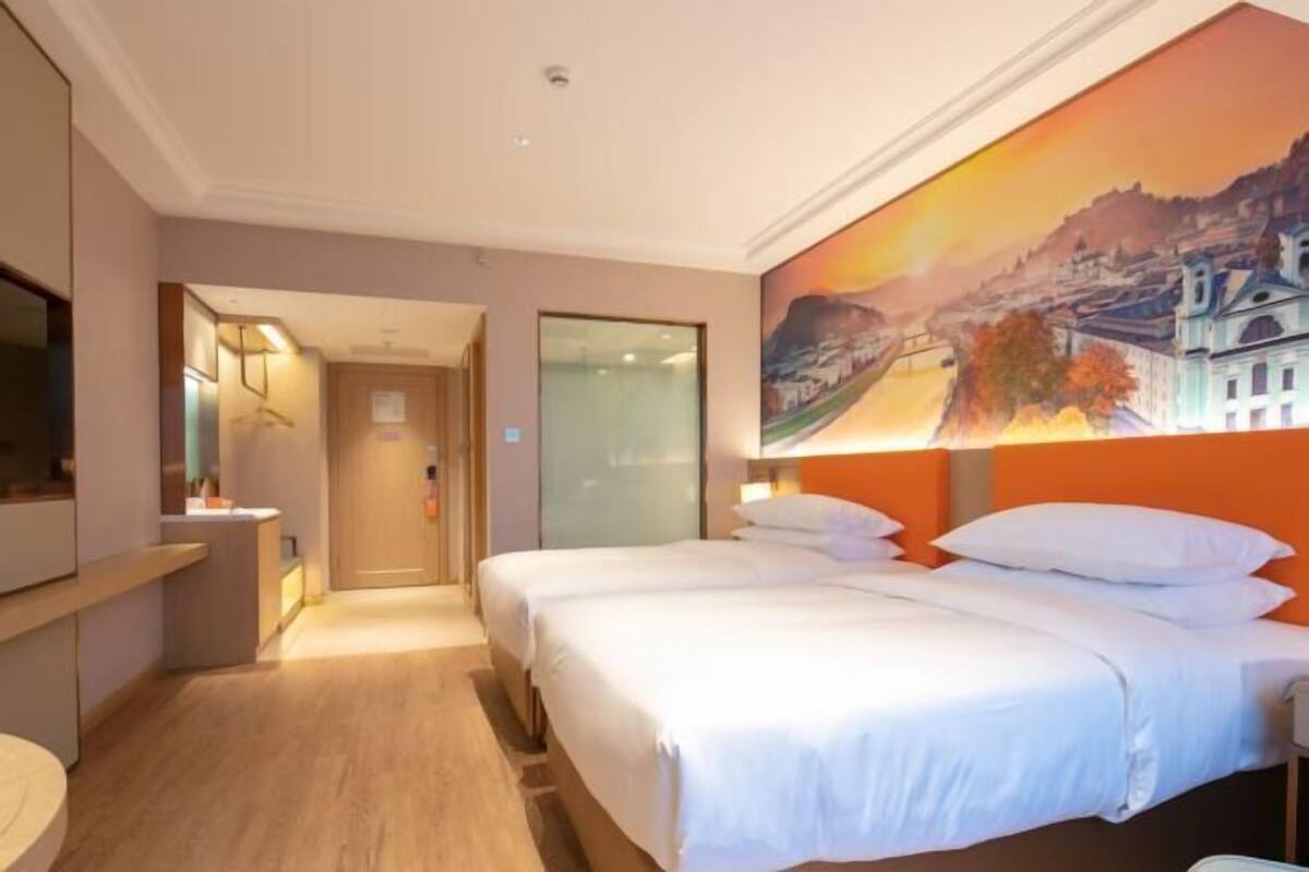 A hotel room with two beds, a painting on the wall, a desk with a chair, and a mirror.