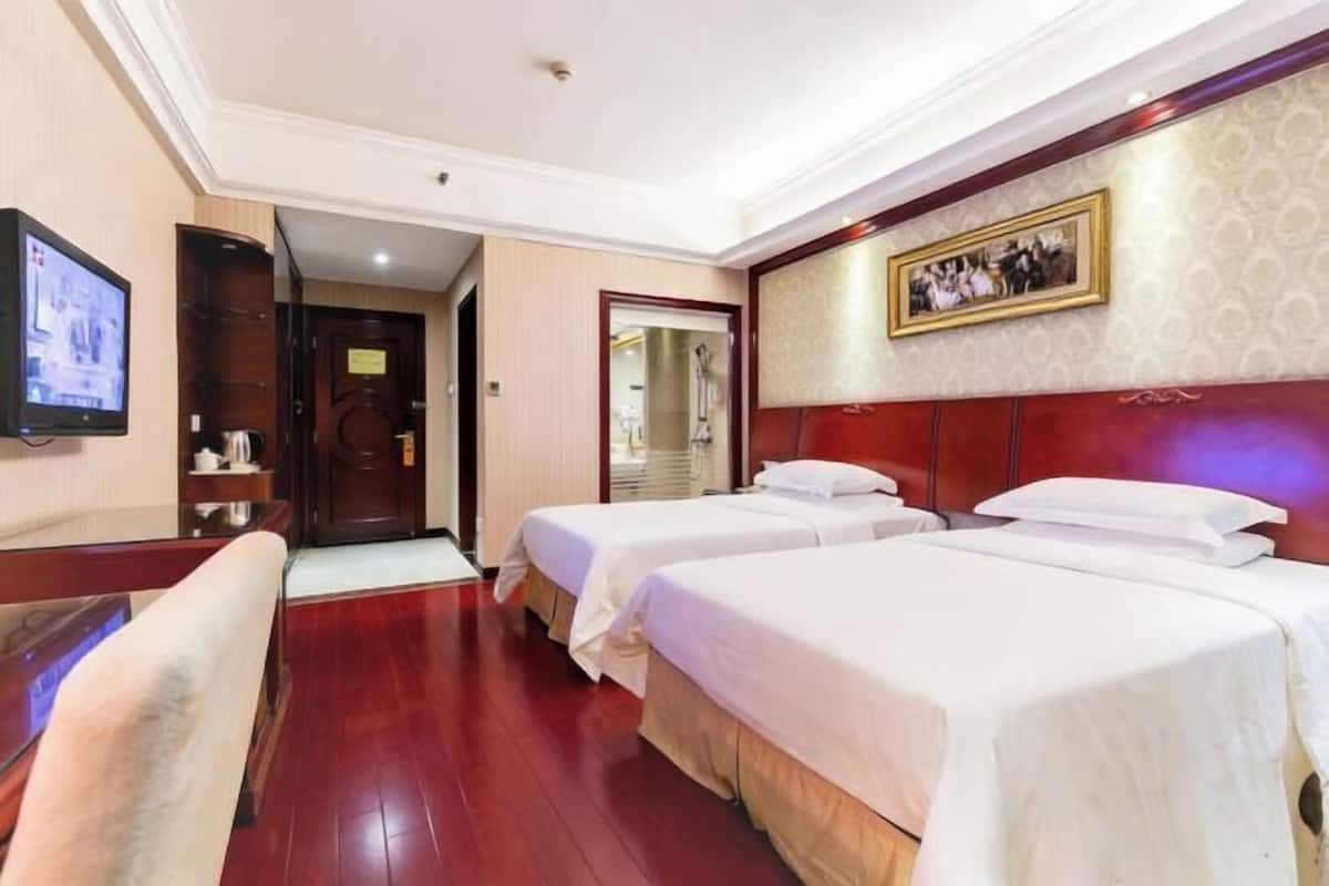 A hotel room with two beds, a television, a wooden floor, and a framed picture on the wall.