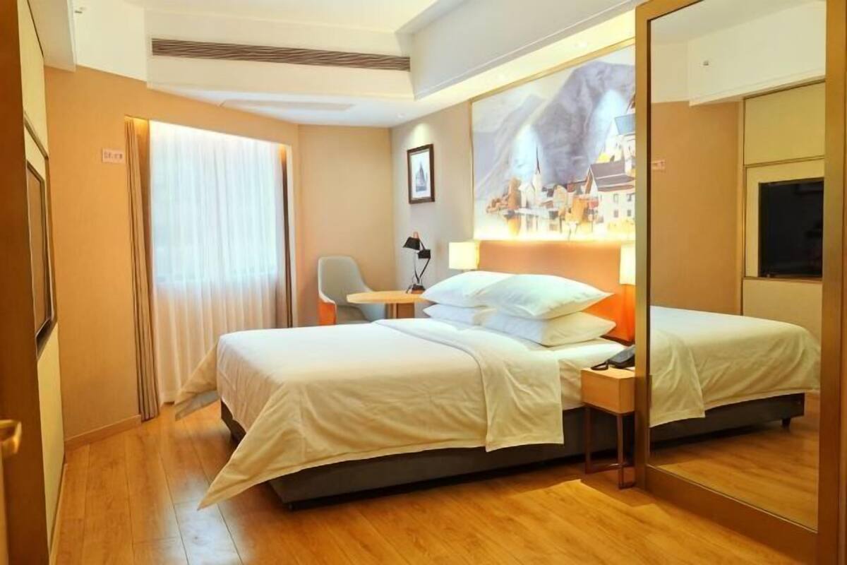 A hotel room with a bed, a desk, a chair, and a mirror.