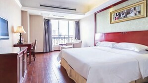 Habitación de hotel con cama, escritorio, silla, televisor y ventana con cortinas.