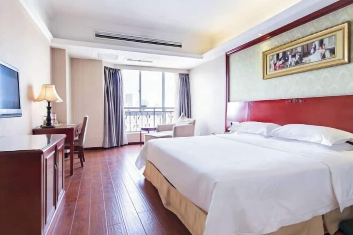 A hotel room with a bed, a desk, a chair, a TV, and a window with curtains.