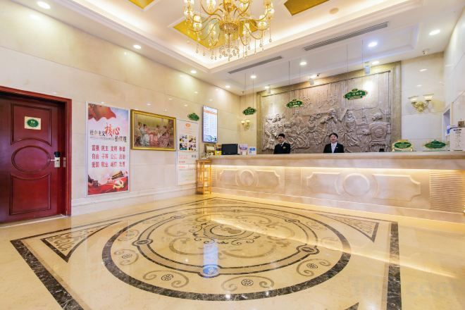 A hotel reception area with a marble floor, a reception desk, and a chandelier.