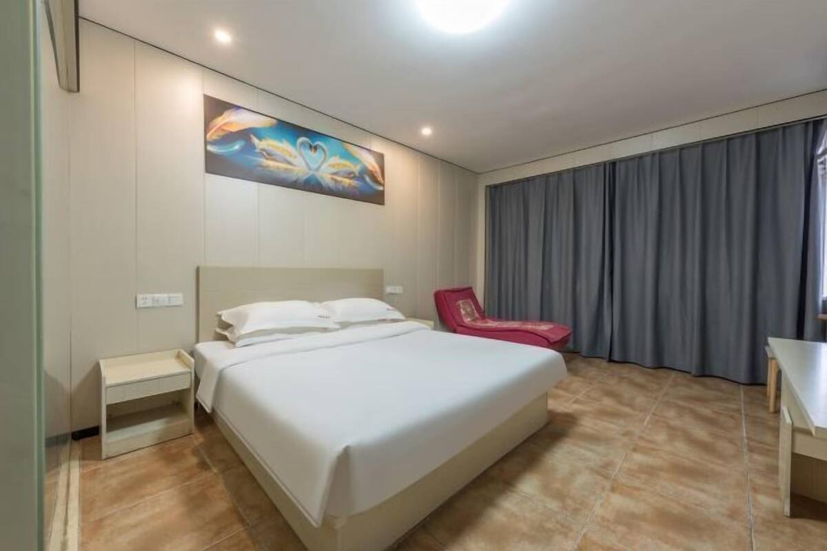 Habitación de hotel con una cama, una silla roja, un escritorio y un cuadro en la pared.