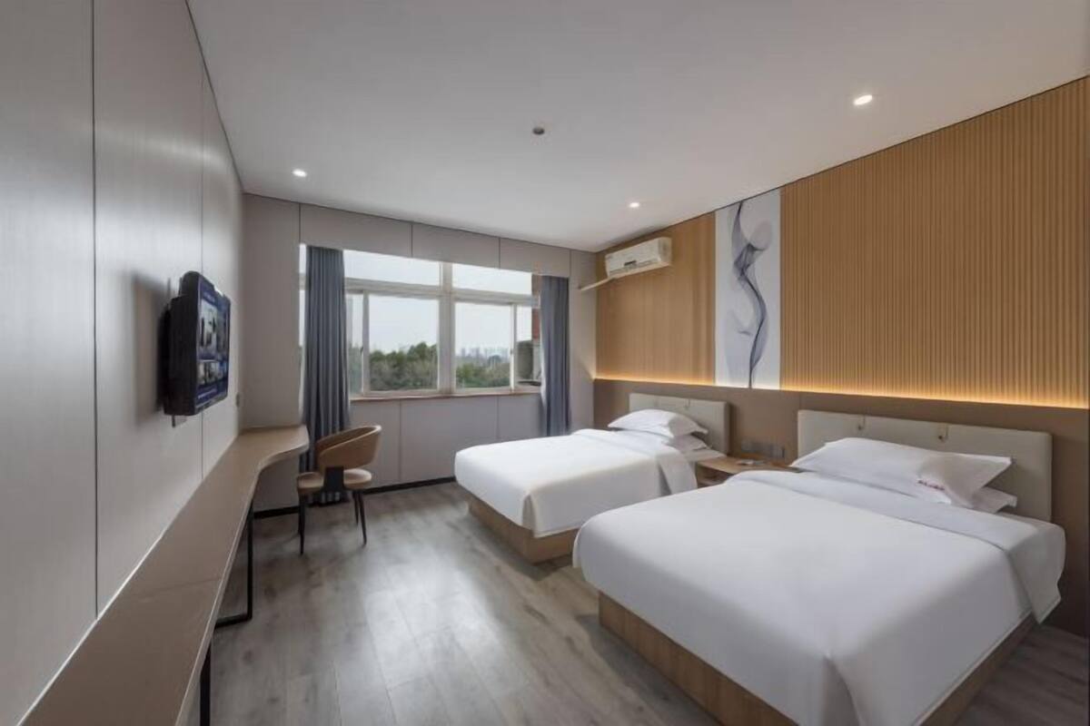 Habitación de hotel con dos camas, un escritorio, una silla y un ventanal grande.