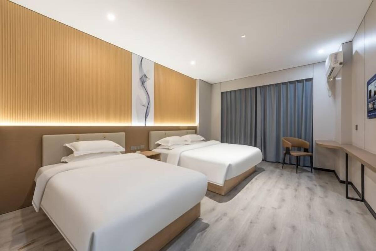 Habitación de hotel con dos camas, un escritorio, una silla y un ventanal con cortinas.