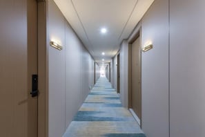 Un corridoio d'hotel con porte su entrambi i lati, pavimento rivestito di moquette e illuminazione a soffitto.