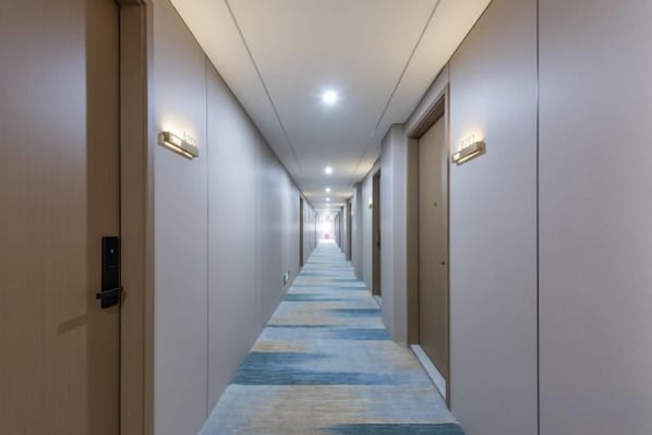 A hotel corridor with doors on both sides, a carpeted floor, and overhead lighting.