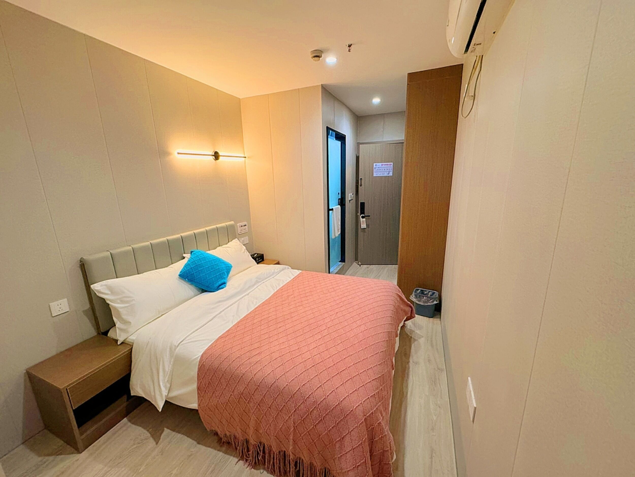 A hotel room with a bed, bedside table, and a wall-mounted light fixture.