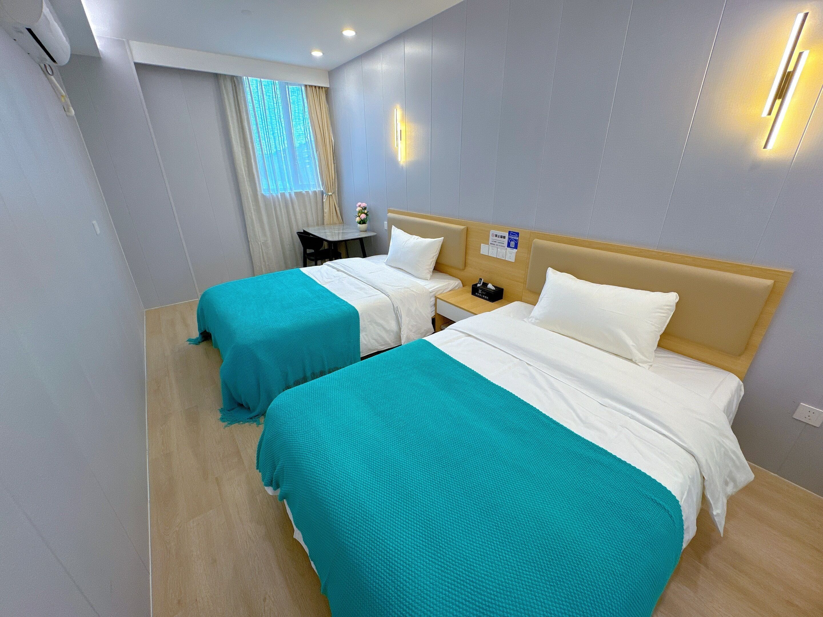 A hotel room with two beds, a small table, and a window with curtains.
