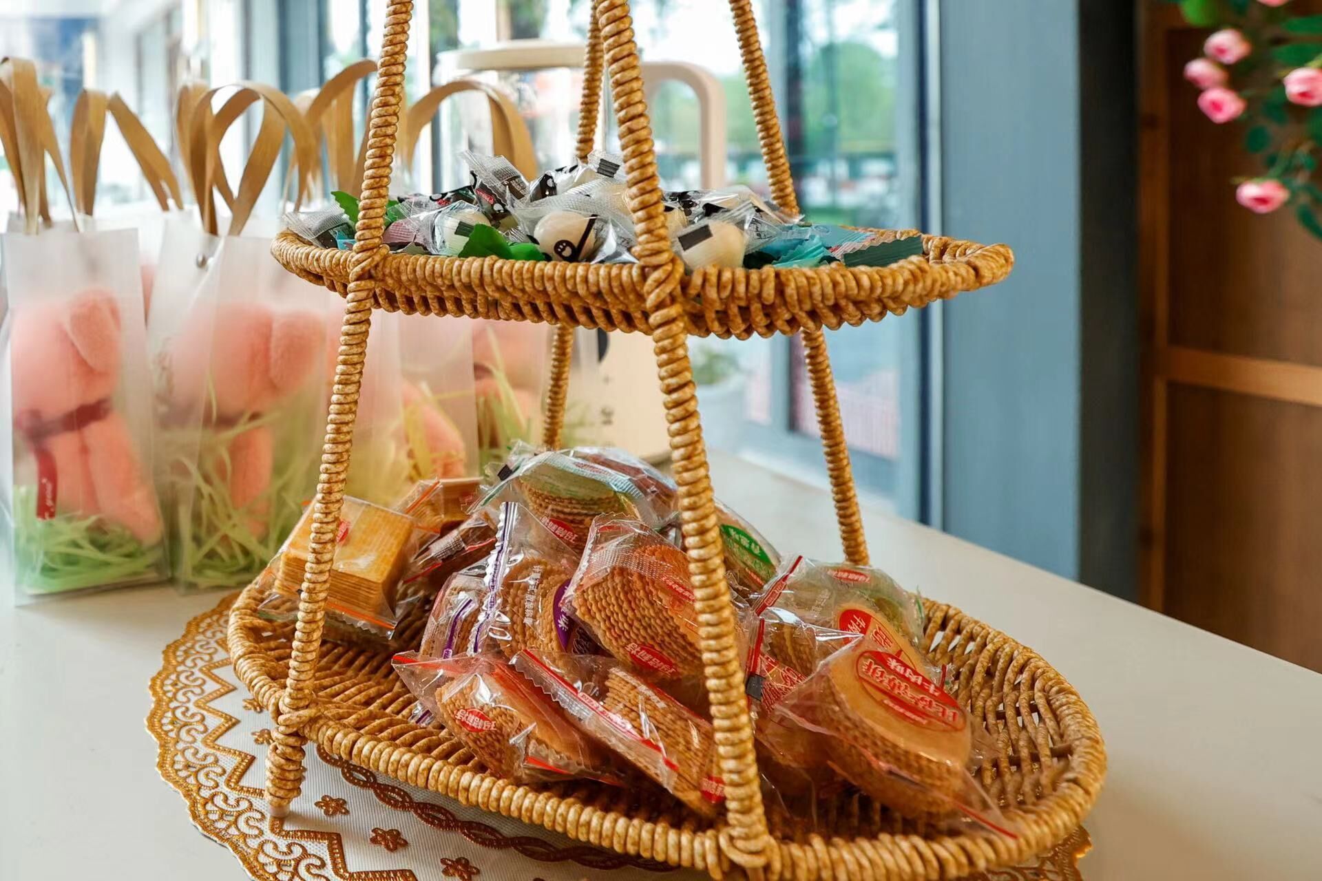 Una cesta de mimbre de tres niveles llena de bocadillos envasados y un objeto decorativo sobre una mesa.