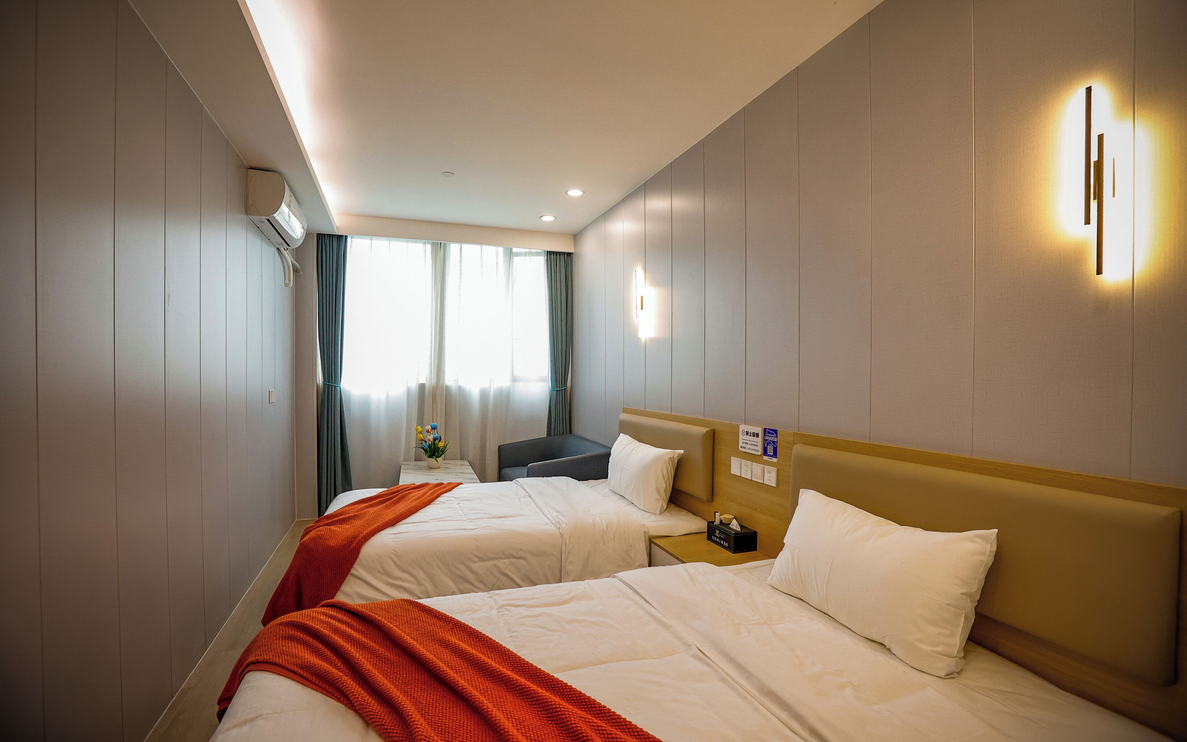 Een hotelkamer met twee bedden, een tafeltje, een stoel en een raam met gordijnen.