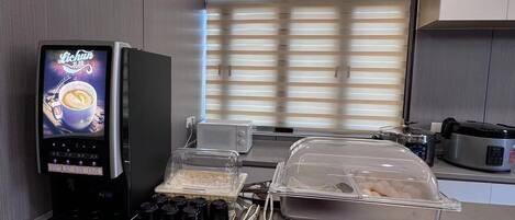 A modern kitchen with a coffee machine, a food display, and a window with blinds.