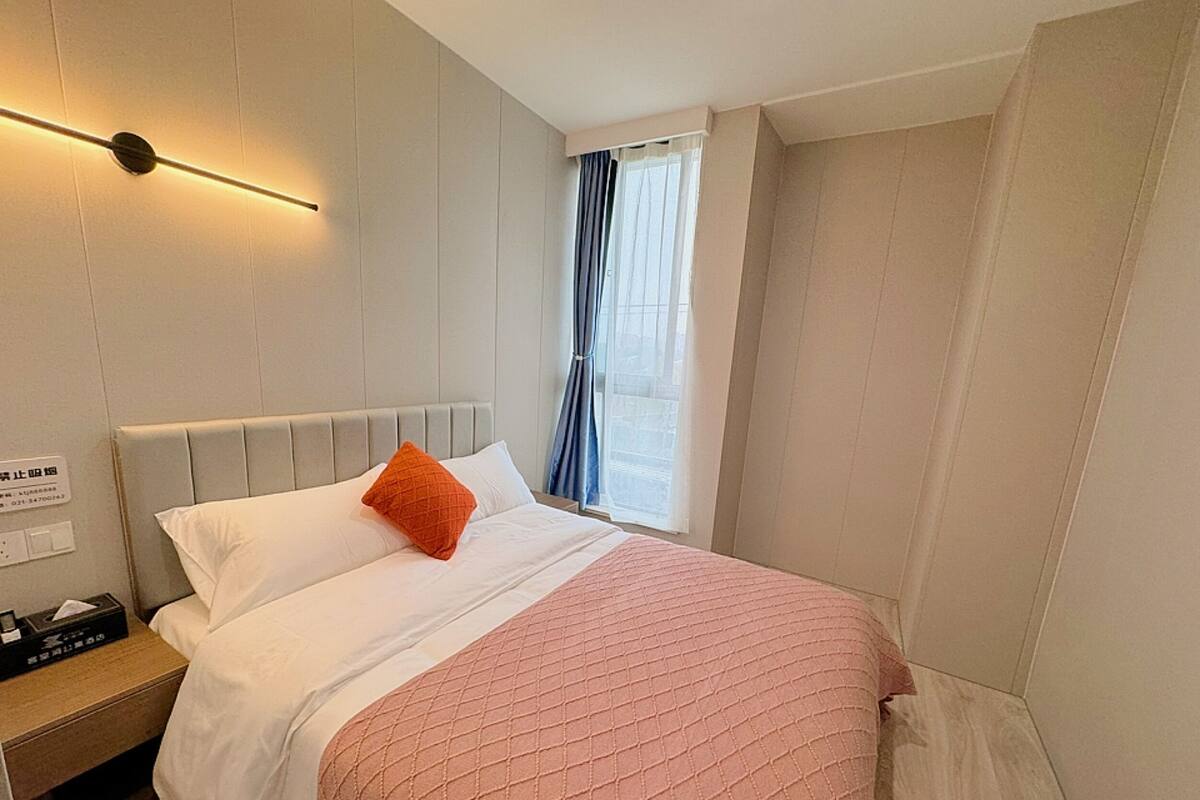 A hotel room with a bed, a nightstand, a lamp, and a window with curtains.