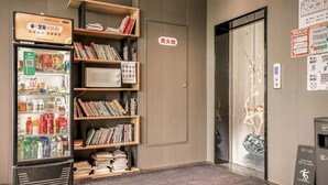 A hotel lobby with a vending machine stocked with snacks and drinks, a bookshelf with books, and an elevator with a sign indicating a wet floor. - Ketangjian Apartment Hotel  (Shanghai)