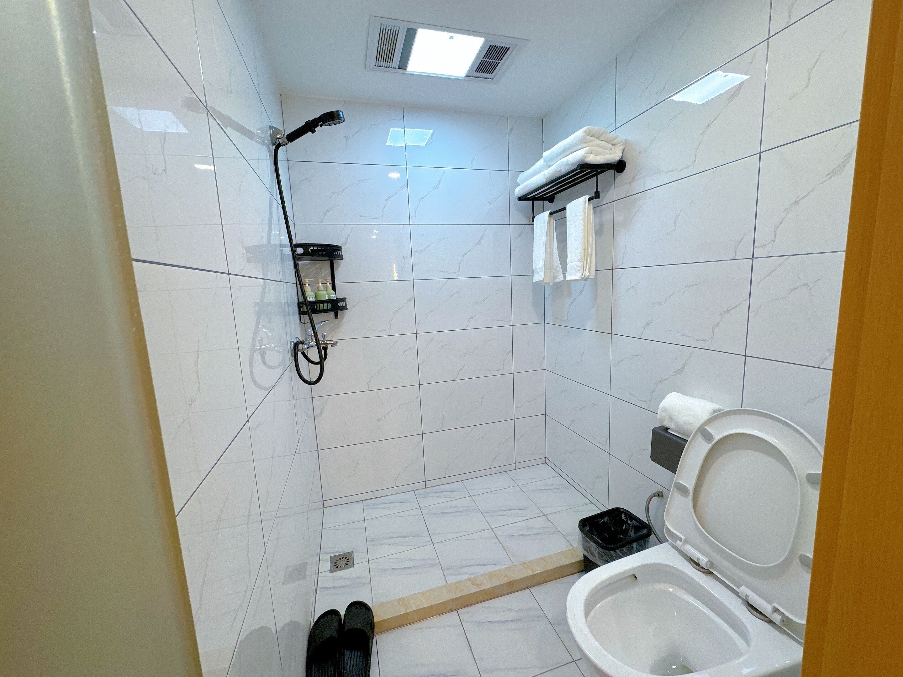 A small bathroom with a shower, toilet, and a shelf with toiletries.
