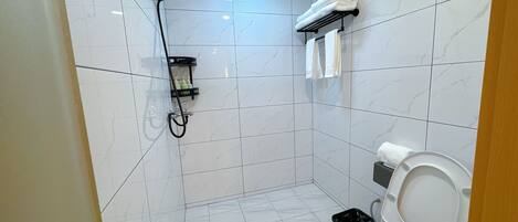 A small bathroom with a shower, toilet, and a shelf with toiletries.