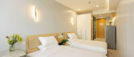 A hotel room with two beds, a small table with a vase of flowers, and a refrigerator.