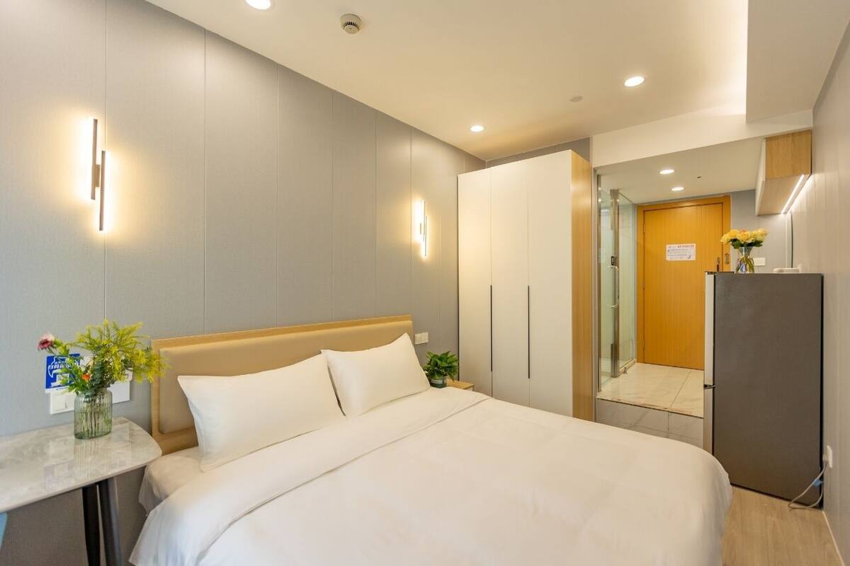 A modern hotel room with a large bed, bedside tables, a wardrobe, and a shower area.