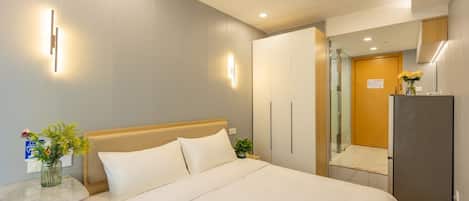 A modern hotel room with a large bed, bedside tables, a wardrobe, and a shower area.