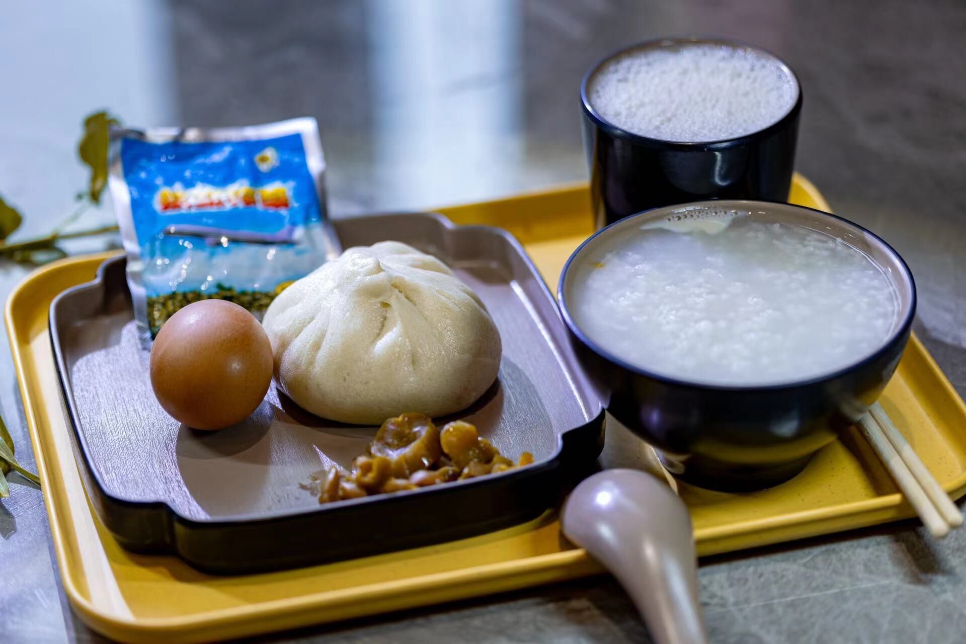A tray with a steamed bun, a bowl of soup, a packet of instant noodles, and a cup of tea.
