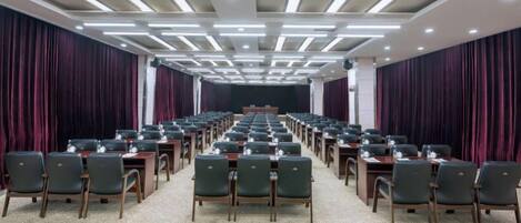A conference room with rows of tables and chairs, a stage at the front, and a patterned carpet.