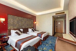 Ein Hotelzimmer mit zwei Betten, einem Fernseher, einem Schreibtisch und einer Badezimmertür.