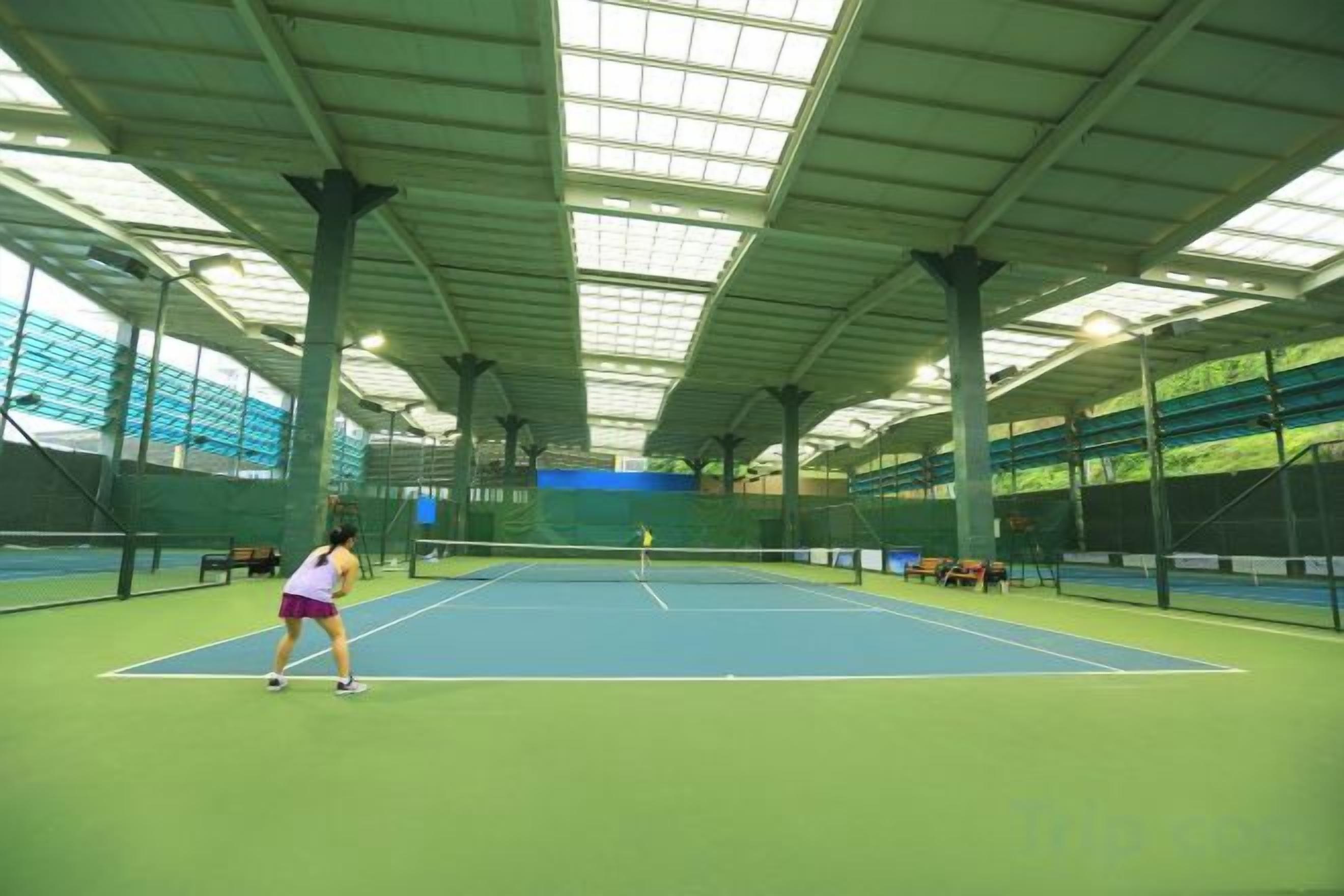 An indoor tennis court with a net, benches, and a high ceiling.