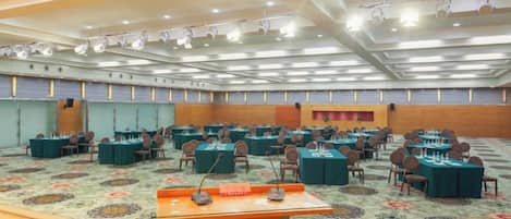 Un salón de conferencias con varias mesas y sillas, un atril y piso alfombrado.
