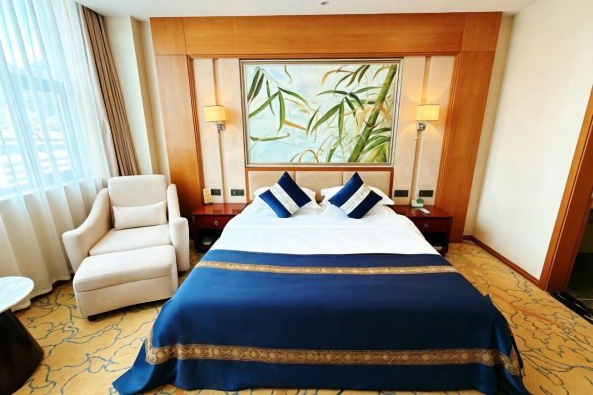 A hotel room with a large bed, a chair, a lamp, and a painting on the wall.