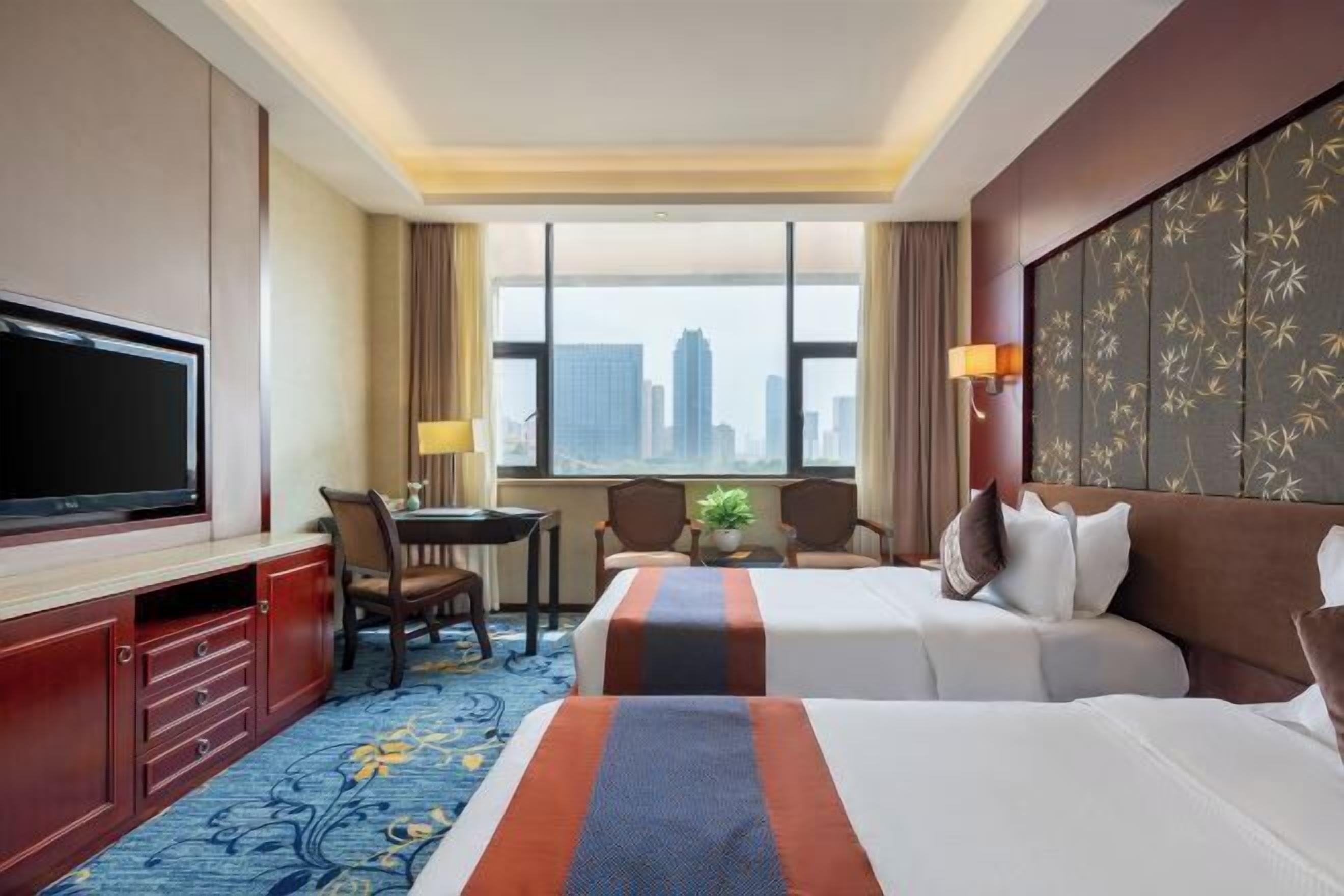 Quarto de hotel com duas camas, uma escrivaninha, uma TV e vista para a cidade.