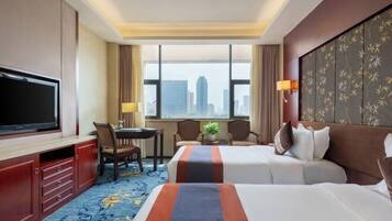 Quarto de hotel com duas camas, uma escrivaninha, uma TV e vista para a cidade.
