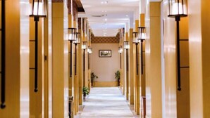 A hotel corridor with a central walkway flanked by columns and wall-mounted lamps. - Jinyang Hotel (Exhibition Center Store)） (Guiyang)