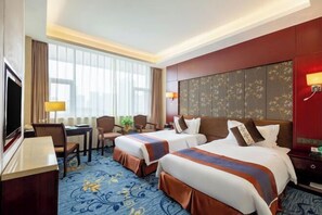 Ein Hotelzimmer mit zwei Betten, einem Schreibtisch, einem Fernseher und einem großen Fenster.