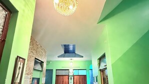 A hallway with green walls, a chandelier, a tiled floor, and a door with a number. - Anukampa Guest House (Agra)