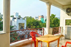 A balcony with a table and chairs, a decorative railing, and a view of buildings and trees.