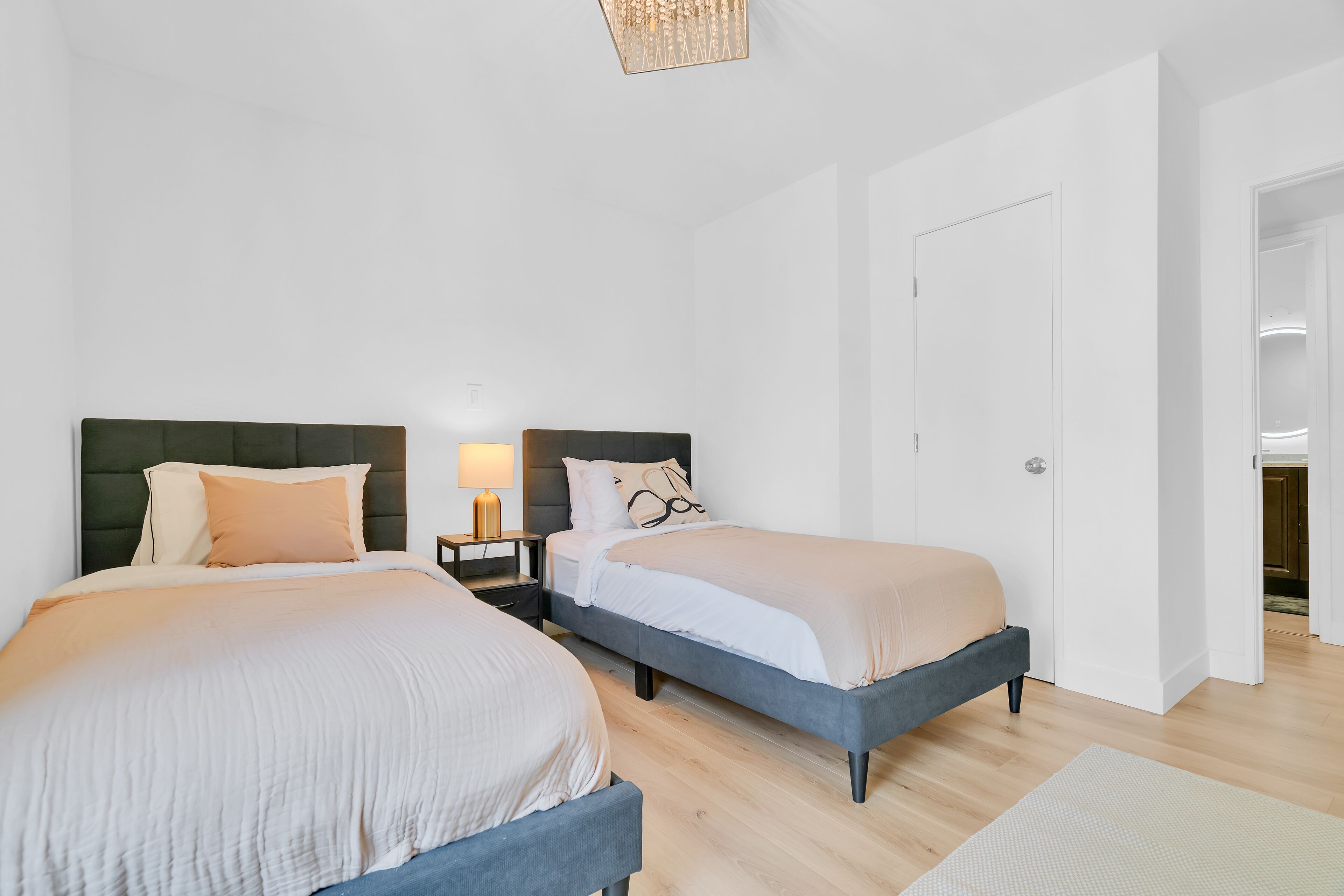 Een slaapkamer met twee bedden, een nachtkastje met een lamp, en een deur naar een andere kamer.
