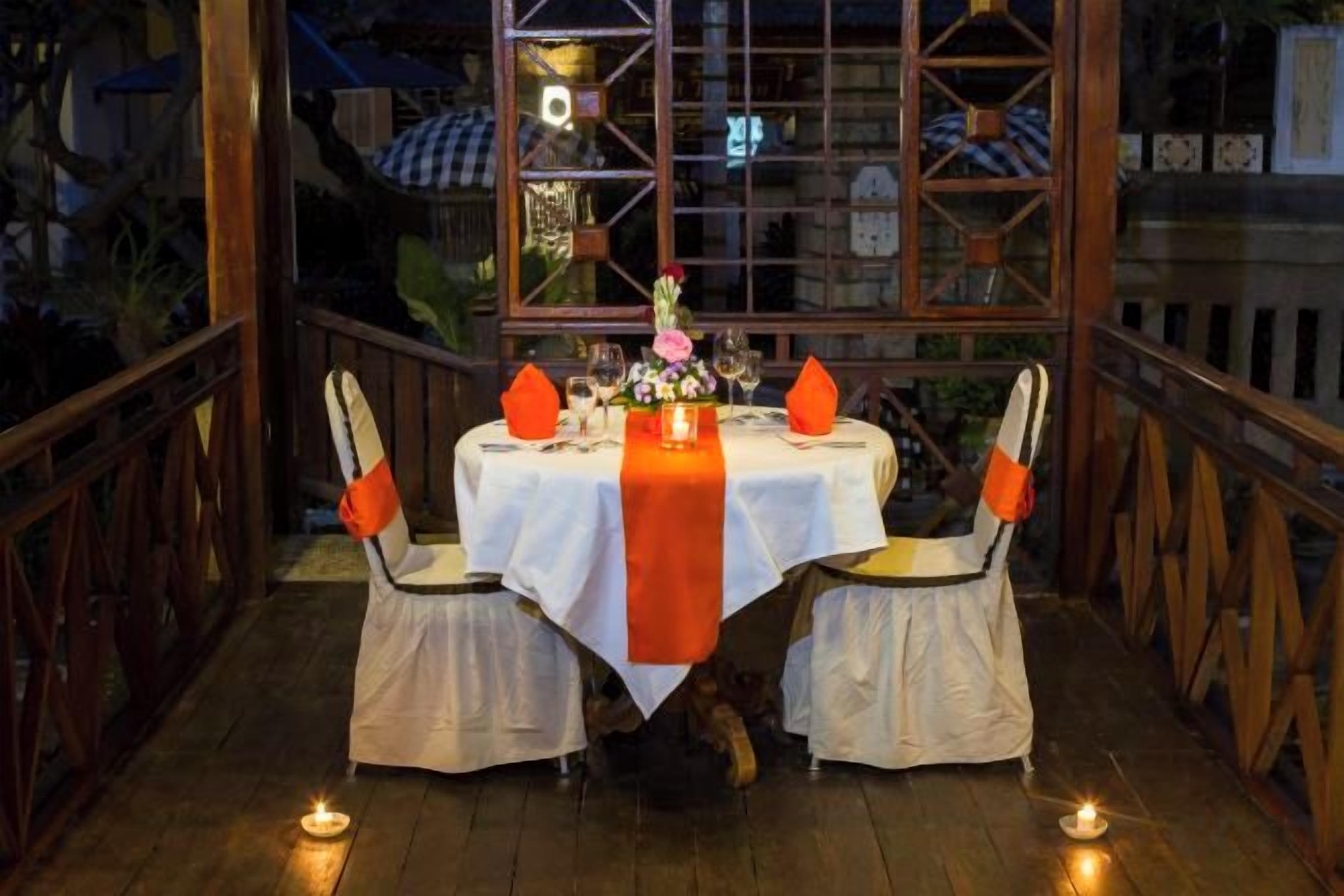 A table set for two with a white tablecloth, orange napkins, and candles.