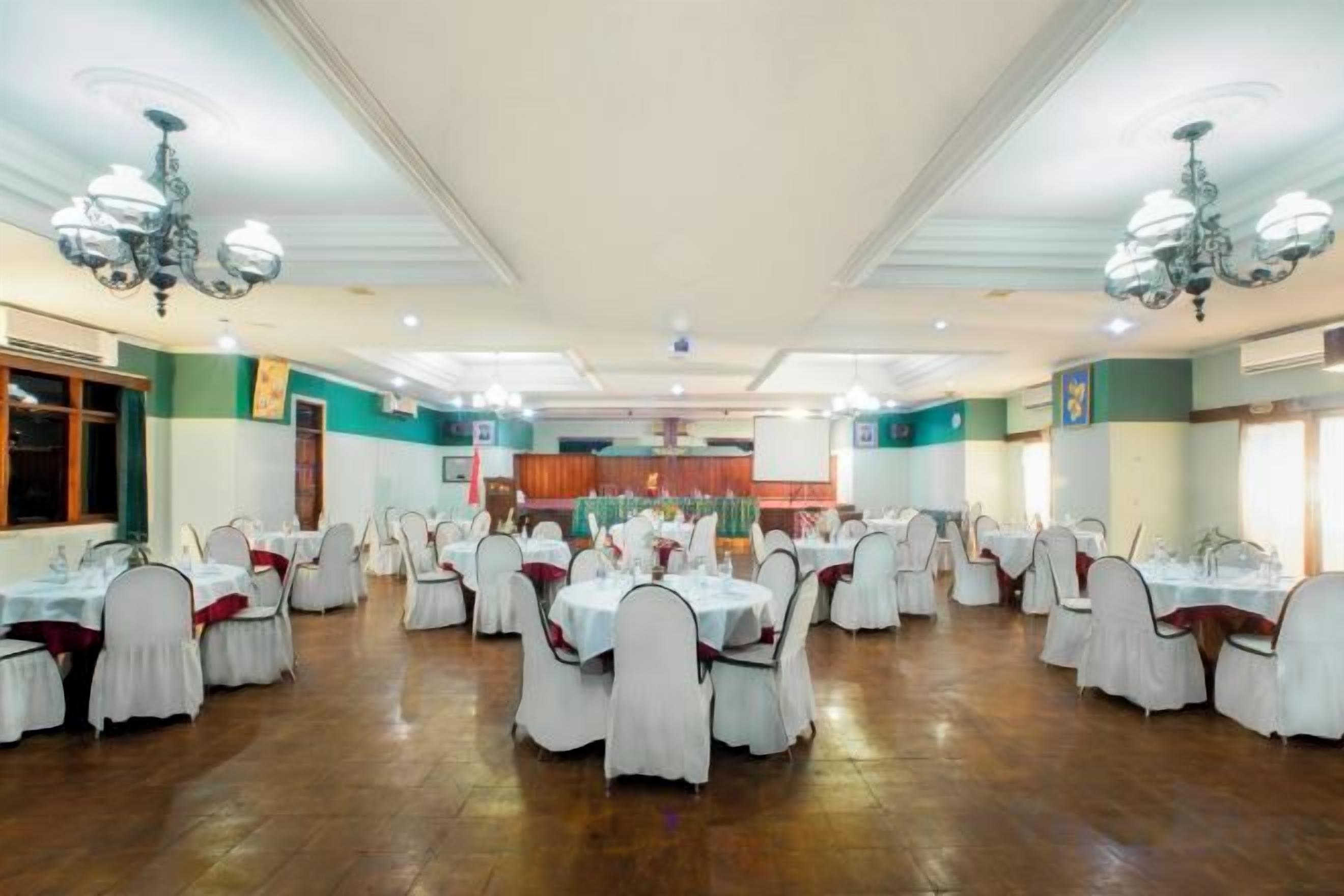 Un salón de banquetes con mesas y sillas redondas, piso de madera y una lámpara de araña.